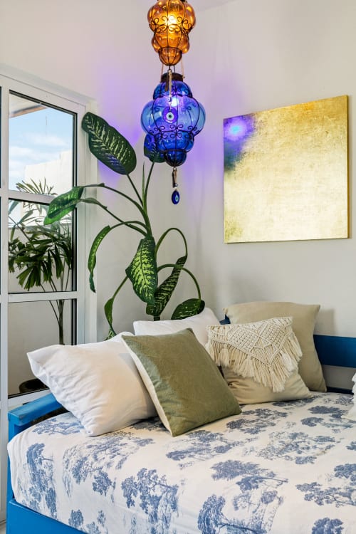 Cozy ocean front cottage bedroom in Isla Mujeres with decorative blue pendant lamp, potted plant, and sea view balcony access
