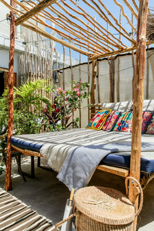 Wooden canopy bed with colorful pillows on oceanfront patio at Isla Mujeres Realty cottage, surrounded by tropical plants