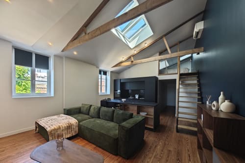 Studio loft moderne à l'hôtel O LIT avec canapé vert, puits de lumière, poutres apparentes, kitchenette et mur d'accent foncé