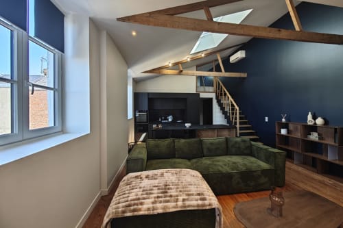 Appartement loft moderne à O LIT avec canapé vert, poutres apparentes, verrière, cuisine noire et escalier bois en France