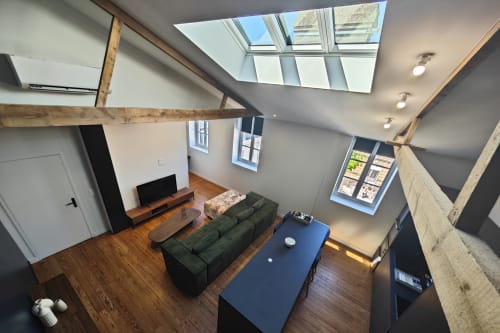 Studio loft moderne à l'hôtel O LIT en France avec puits de lumière, poutres en bois, canapé vert et parquet