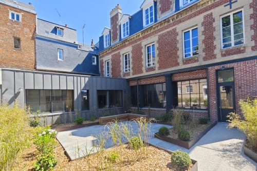 Cour du O LIT en France avec extension moderne en noir, grandes baies vitrées, bâtiments en brique et jardin aménagé