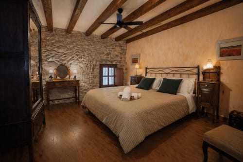Dormitorio rústico en Casa Rural Cal París con paredes de piedra, vigas de madera, cama doble y decoración tradicional en La