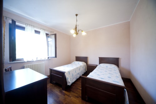 Deux lits jumeaux dans une chambre lumineuse de la villa Agriturismo Buriano, avec parquet, fenêtres et luminaire suspendu