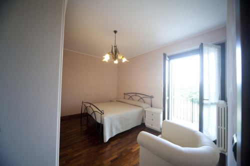 Chambre lumineuse à l'Agriturismo Buriano à Lubriano avec lit double, fauteuil blanc et balcon surplombant les jardins