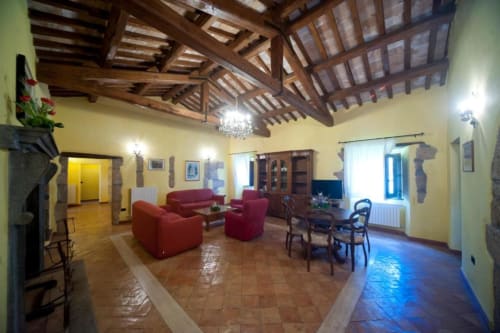 Ampio soggiorno dell'appartamento La Quercia ad Agriturismo Buriano con sedute rosse, travi in legno e pavimenti in cotto.