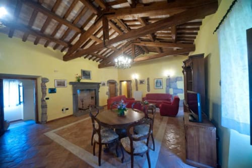 Ampio soggiorno dell'appartamento La Quercia in Agriturismo Buriano con travi in legno a vista, tavolo rotondo e divani rossi