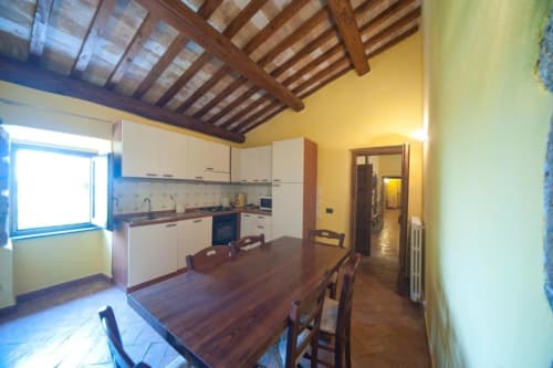 Ampia zona cucina-living nell'appartamento La Quercia di Agriturismo Buriano con travi in legno, pareti gialle e vista sul giardino