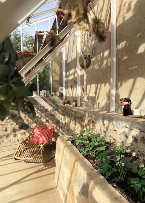 Cour ensoleillée de la Maison Mansel avec plantes en pot, macramés suspendus et jardinières en pierre