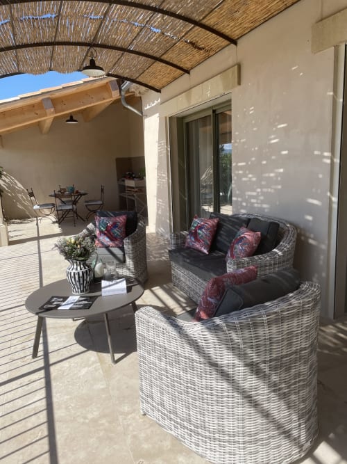 Sonnige Terrasse des Landhauses Gordes mit Korbmöbeln, farbigen Kissen, kleinem Tisch und strohgedeckter Pergola