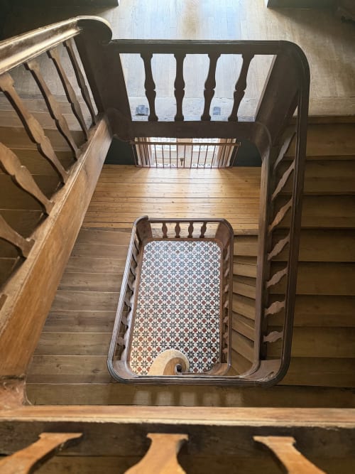 Vue de dessus d'un escalier en bois à la Maison Mansel B&B à Mesnil-en-Ouche, avec carrelage à motifs visible au sol.