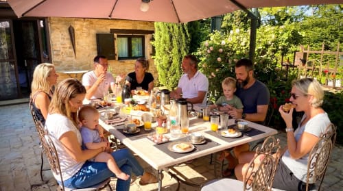 Family and guests dining outdoors under pink umbrella at Le Clos Des Anges B&B in Bagnols, France