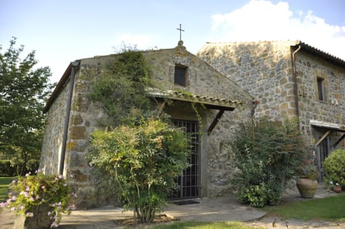 Steinkapelle mit Kreuz im Agriturismo Buriano, ein rustikales italienisches Gästehaus in Lubriano, umgeben von Efeu und Garten.