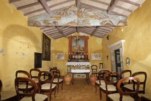 Historische Kapelleninterieur des Agriturismo Buriano in Lubriano mit gelben Wänden, Holzbalken, Altar und hölzernen Stühlen