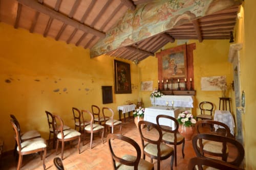 Historische Kapelle im Agriturismo Buriano in Lubriano, Italien, mit gelben Wänden, Holzbalken und rustikalen Holzstühlen