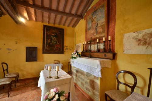 Kapelle des Agriturismo Buriano mit gelben Wänden, Altar, Kerzen und Fresken in Lubriano, Italien