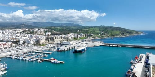 Cité portuaire méditerranéenne côtière avec bâtiments blancs, eaux bleues et montagnes vertes près d'El Ghazouane, Maroc