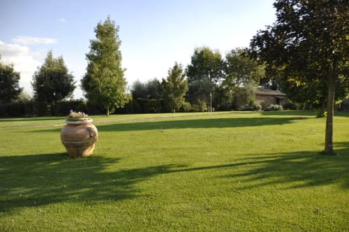 Weitläufiger grüner Rasen im Agriturismo Buriano mit Terrakotta-Urne, alten Bäumen und toskanischer Villa im Hintergrund