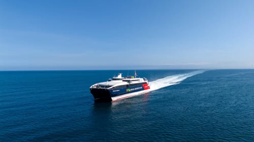Navire ferry haute vitesse traversant les eaux océaniques bleues avec éclaboussures de sillage visibles