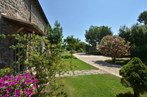 Agriturismo Buriano: Steingebäude mit magentafarbener Bougainvillea, gepflegten Gärten und baumgesäumter Zufahrt in Lubriano