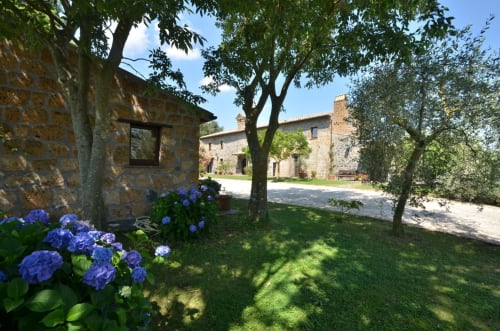 Innenhof des Agriturismo Buriano in Lubriano mit Steingebäuden, blauen Hortensien und Schattenbäumen