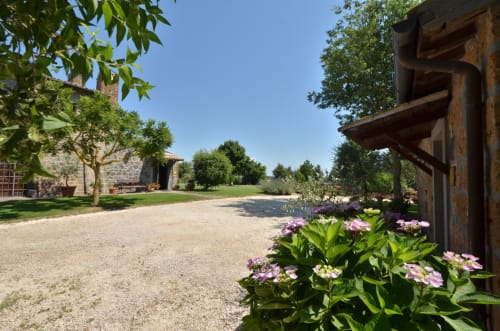 Toskanischer Agriturismo-Innenhof mit rosa Blüten, Steingebäuden und baumbestandenem Gelände im Agriturismo Buriano in Lubriano