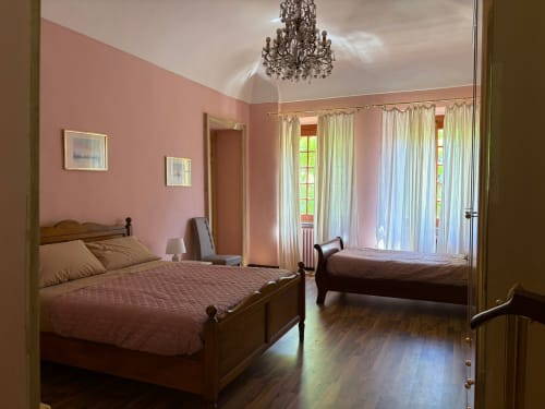 Due letti in legno con biancheria bordeaux in una camera da letto rosa brillante della Villa Mirano B&B a Piossasco, con lampadario e giardino