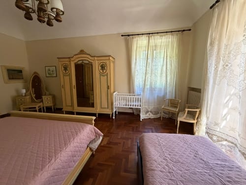 Camera elegante presso Villa Mirano B&B con due letti, armadio antico, culla bianca e tende color crema