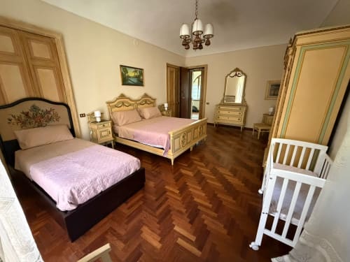 Spaziosa camera familiare alla Villa Mirano B&B a Piossasco con due letti, arredamento classico, pavimento a spina di pesce e lettino.