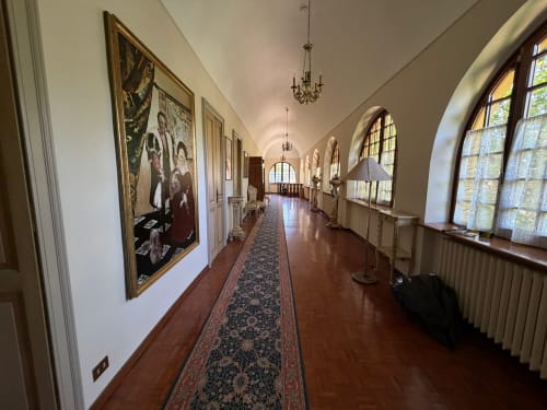 Elegante corridoio della Villa Mirano B&B a Piossasco con finestre ad arco, opere d'arte incorniciate e tappeto corridoio decorativo
