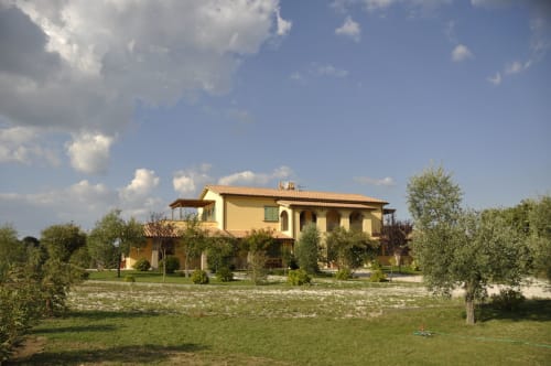 Agriturismo Buriano, a yellow Tuscan farmhouse B&B in Lubriano with olive trees and manicured gardens under blue sky