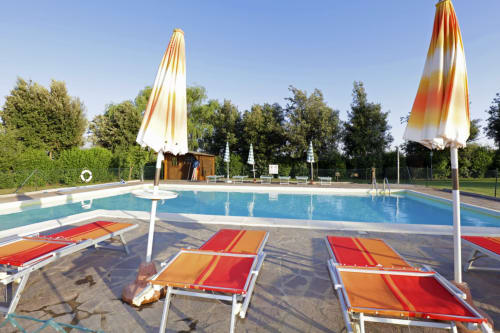 Swimming pool at Agriturismo Buriano with loungers and colorful umbrellas overlooking gardens in Lubriano