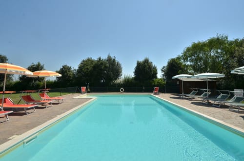 Rectangular swimming pool at Agriturismo Buriano in Lubriano, Italy, surrounded by loungers and umbrellas with lush green