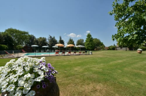 Agriturismo Buriano pool area with white and purple flowers, loungers, umbrellas, and manicured lawn in Lubriano, Italy