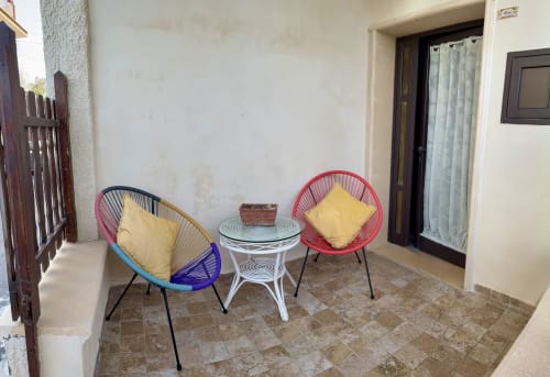Colorful patio seating at Noemi Holiday House in Agnone Bagni with two woven chairs and round table
