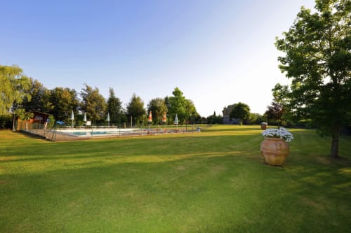 Agriturismo Buriano's lush green grounds with swimming pool, garden planters, and trees in Lubriano, Italy