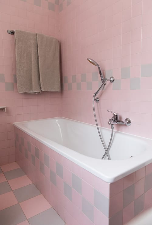 Pink tiled bathroom with white bathtub, handheld showerhead, and beige towels at Cristallo Apartment in Ravenna