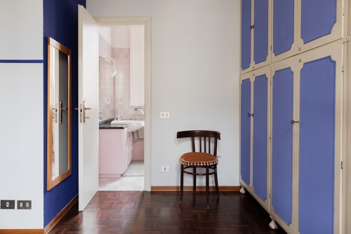 Cristallo Apartment bedroom with blue accent wall, wooden chair, and ensuite bathroom in Ravenna