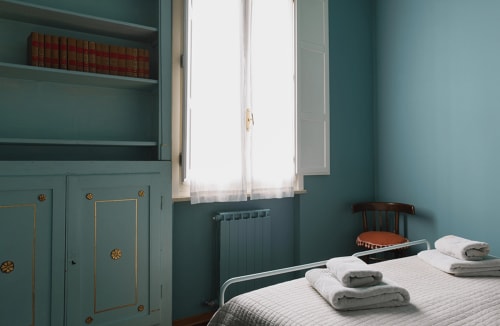 Teal bedroom with made bed, folded towels, vintage wardrobe, and window at Cristallo Apartment, Ravenna
