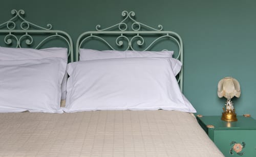 Elegant bedroom at Cristallo Apartment Ravenna with ornate metal bed frame, white pillows, and teal wall with vintage lamp.