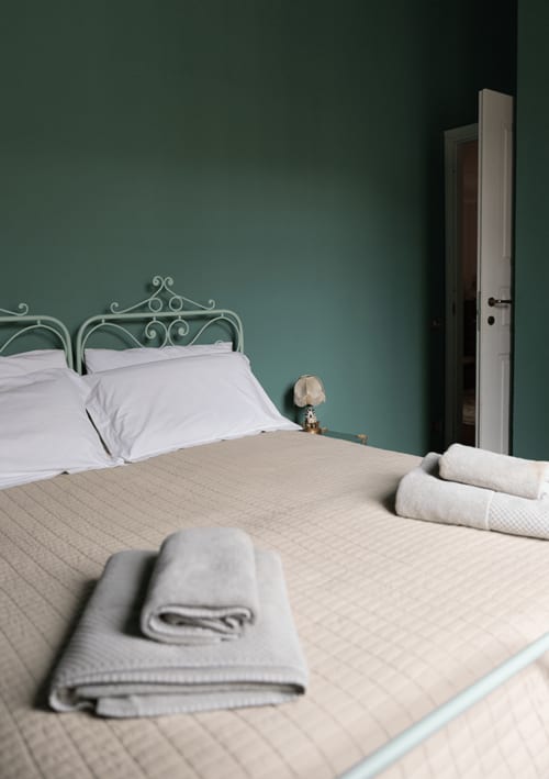 Bedroom at Cristallo Apartment in Ravenna with green walls, metal bed frame, white pillows, and folded towels