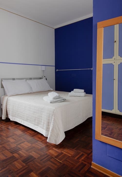 Modern bedroom at Cristallo Apartment in Ravenna with blue accent wall, white bedding, and wooden wardrobe
