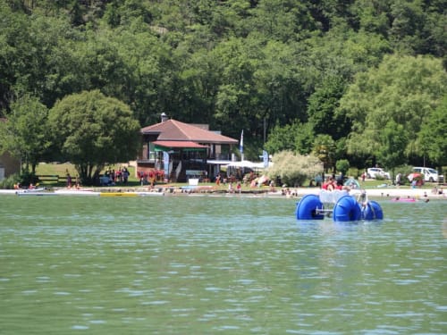 Jouet gonflable bleu sur l'eau au lac de la plage de Vila Cabanes 46, Le Montat, avec pavillon et arbres en arrière-plan