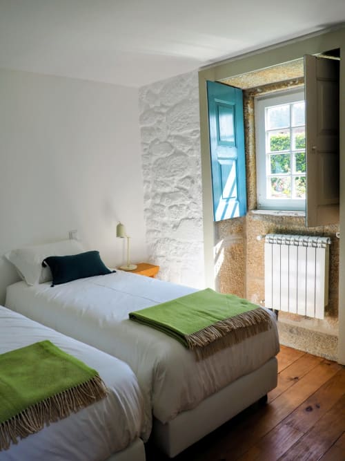 Aconchegante quarto duplo na Quinta da Coutada com paredes de pedra, mantas verdes e janela com vista para a zona rural de Arcos de Valdevez