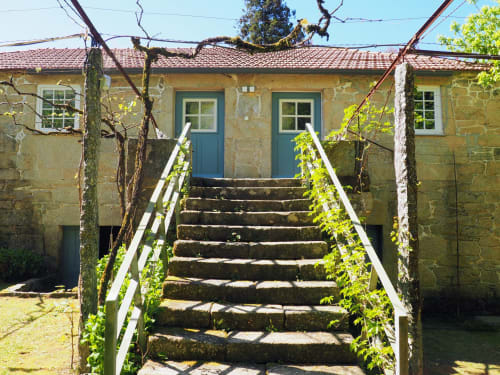 Casa de pedra com portas azuis na Quinta da Coutada, acessada por degraus cobertos de vegetação com corrimãos brancos em Arcos de Valdevez