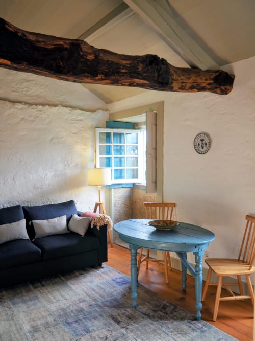 Quarto rústico na Quinta da Coutada com vigas aparentes, mesa azul, sofá preto e paredes caiadas em Arcos de Valdevez