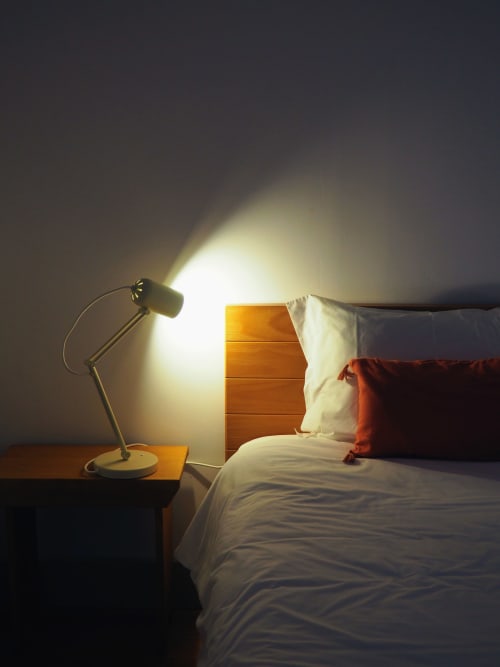 Quarto aconchegante na Quinta da Coutada com luminária acesa na escrivaninha, cabeceira de madeira e roupa de cama branca com almofada vermelha