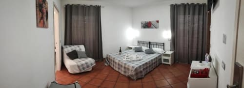 Ampia camera tripla con letto matrimoniale, poltrona, angolo cottura e pavimenti in cotto presso Royal House Fiumicino BnB.