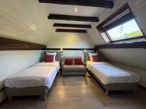 Chambre mansardée lumineuse avec deux lits simples, canapé, poutres en bois et lucarne à l'Hôtel de l'Ange Niedermorschwihr