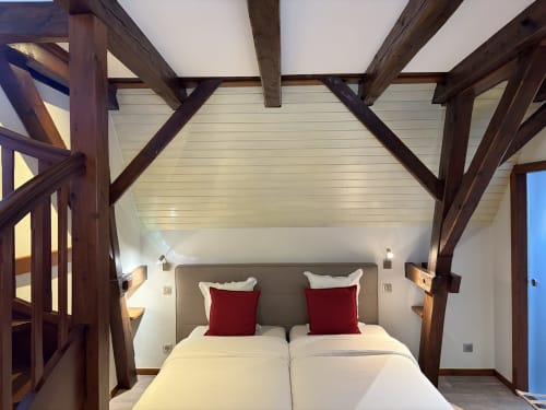Chambre spacieuse à l'Hôtel de l'Ange avec poutres apparentes, lit queen-size, oreillers rouges et vue sur le jardin